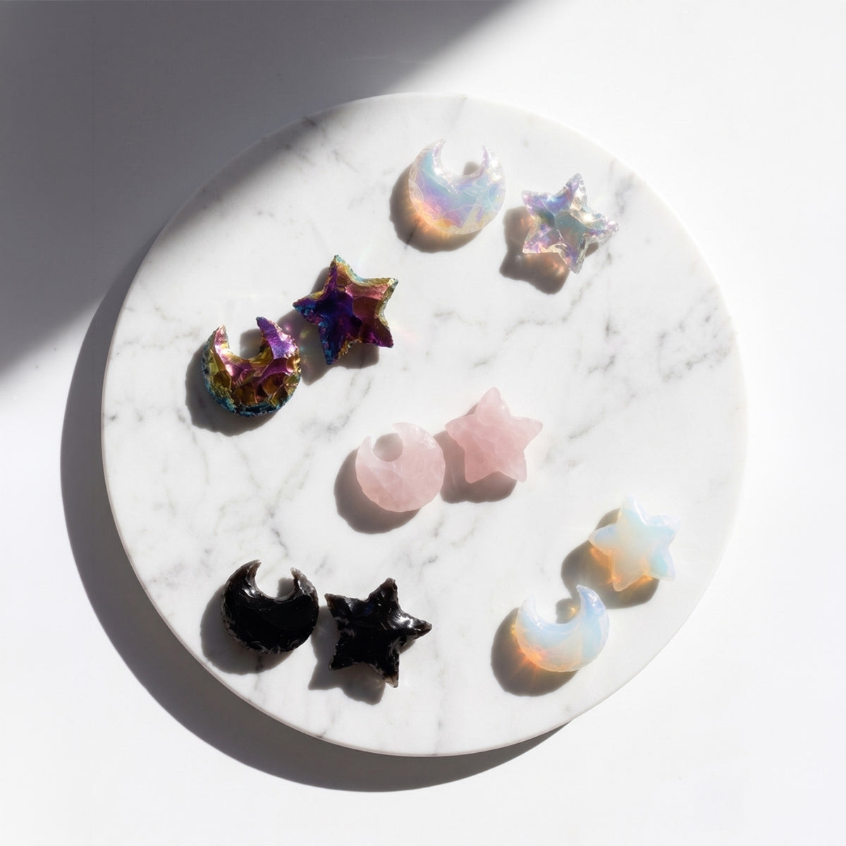 A collection of colorful star and crescent moon jewelry charms arranged on a white marble round tray against a white background with soft shadows.