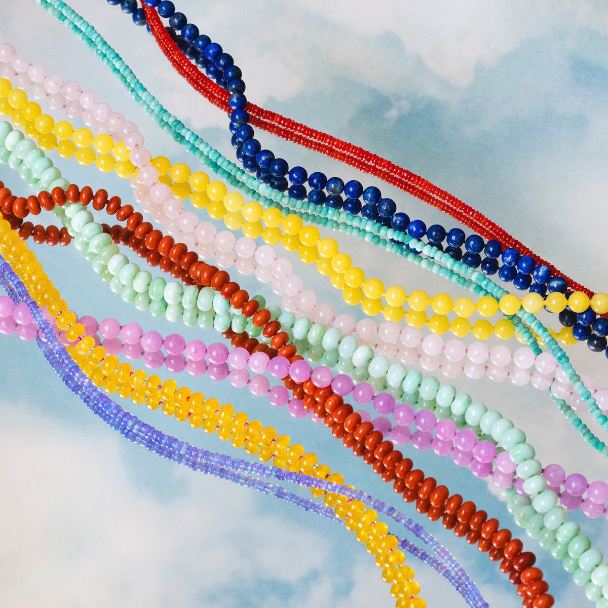 Colourful Anokhi Green gemstone necklace strands arranged on a soft blue background