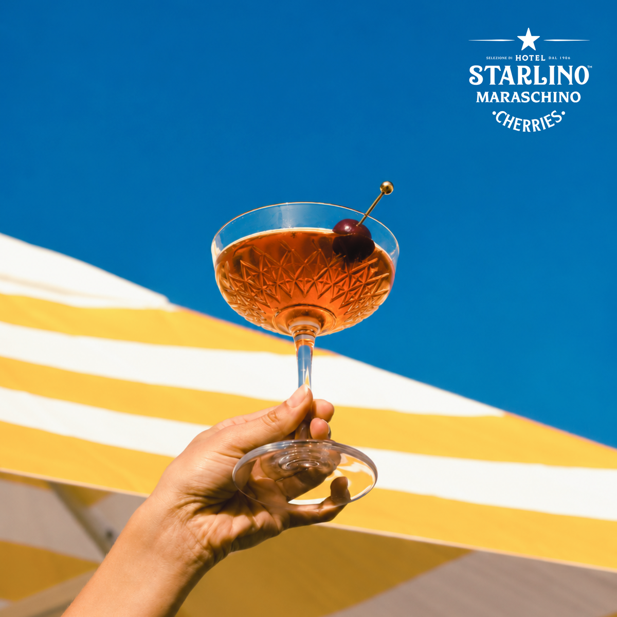 Cocktail garnished with a Hotel Starlino cherry against a blue sky