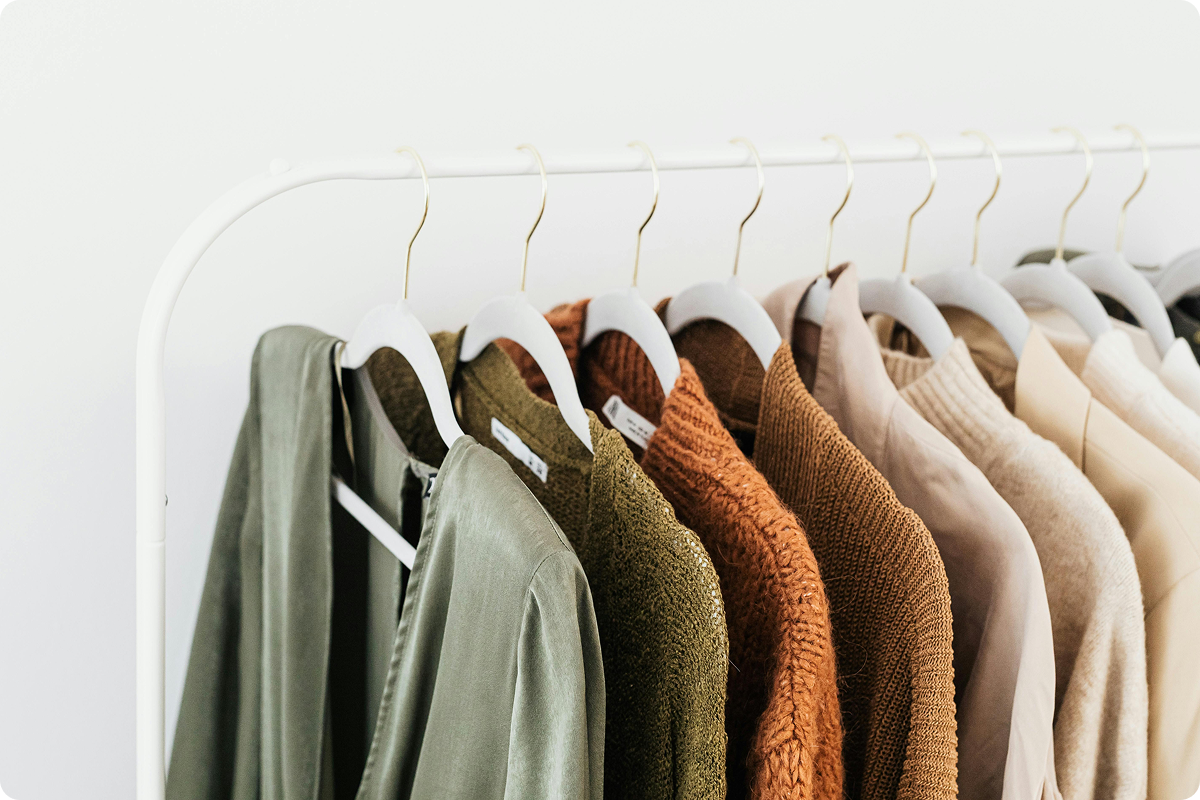 Row of hangers with various colored sweaters on a white rack against a light background